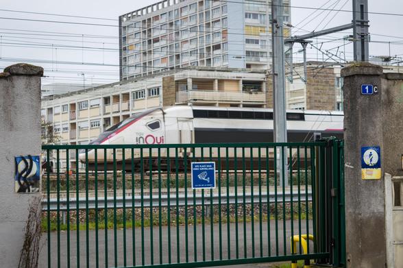 TGV Duplex rolling slowly on a track behind a metal gate in front of it