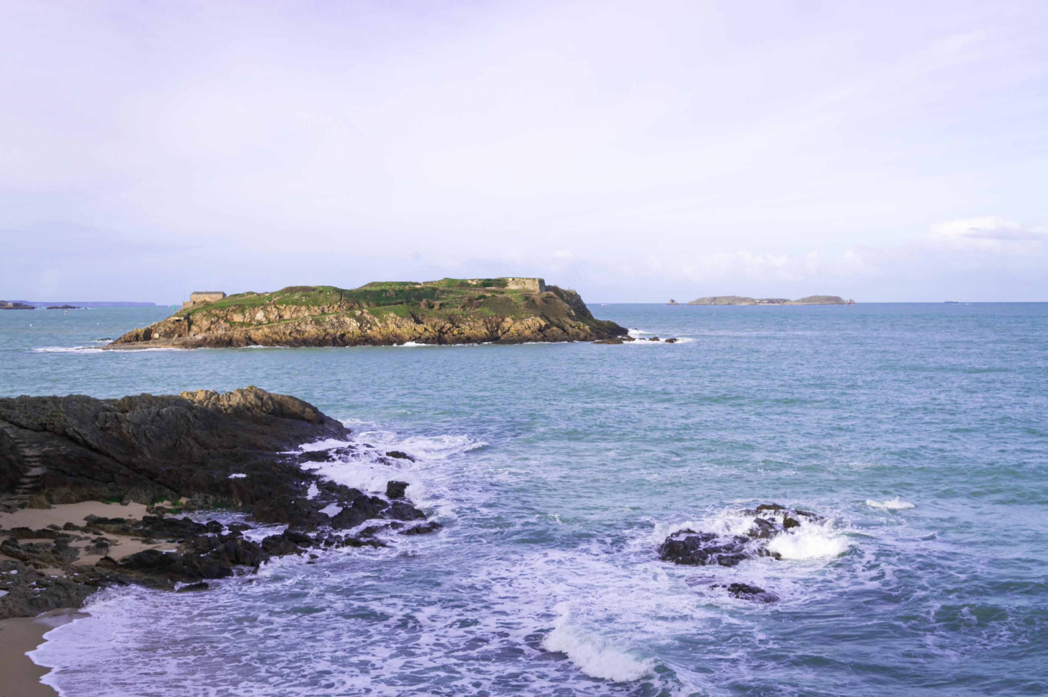 A beach, water hitting rocks near it and some islands in the distance