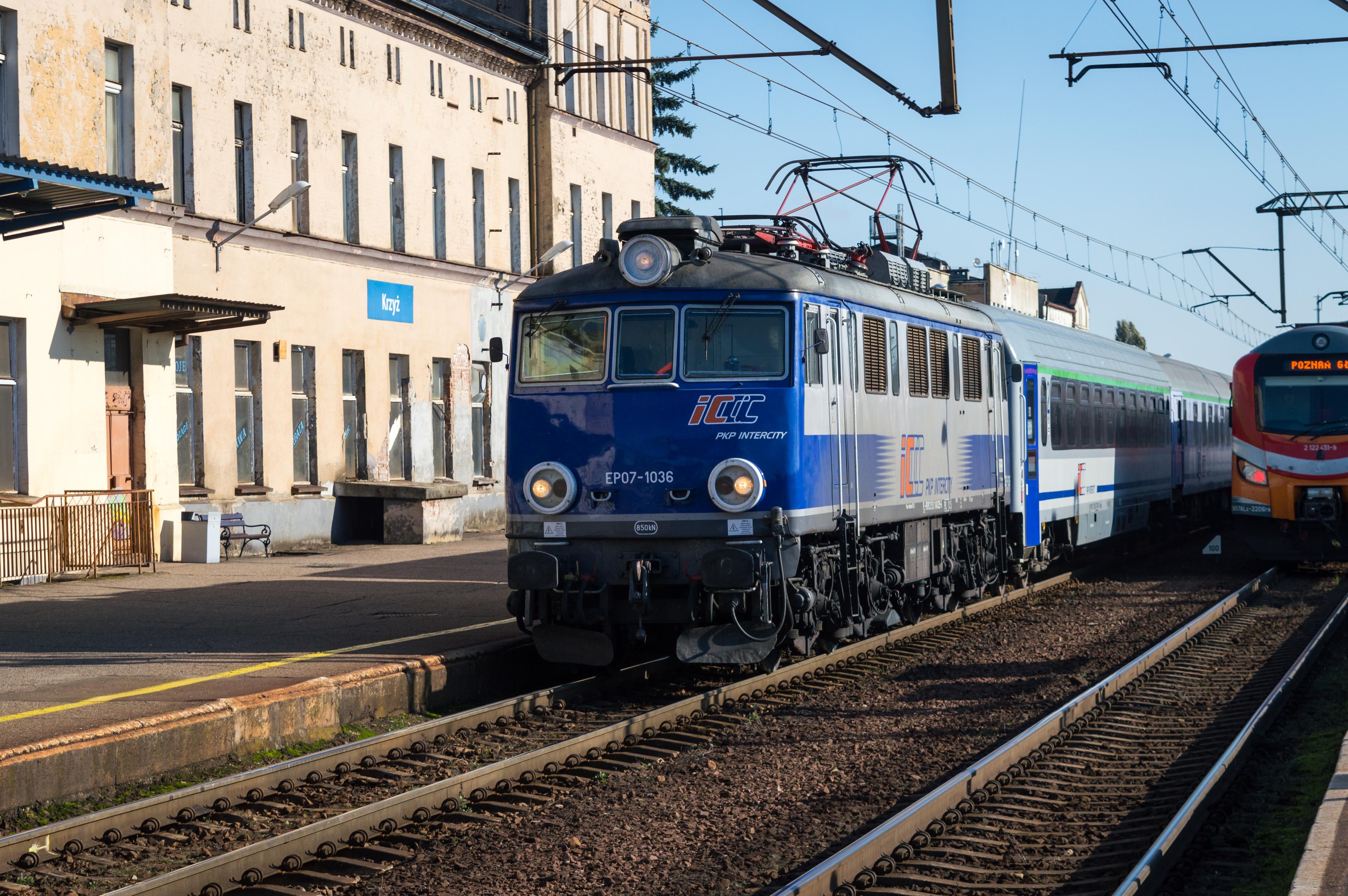 PKP Class EP07 of PKP IC with an IC train passing through Krzyż Wielkopolski station. There is an EN57ALc stopped at a platform right next to it